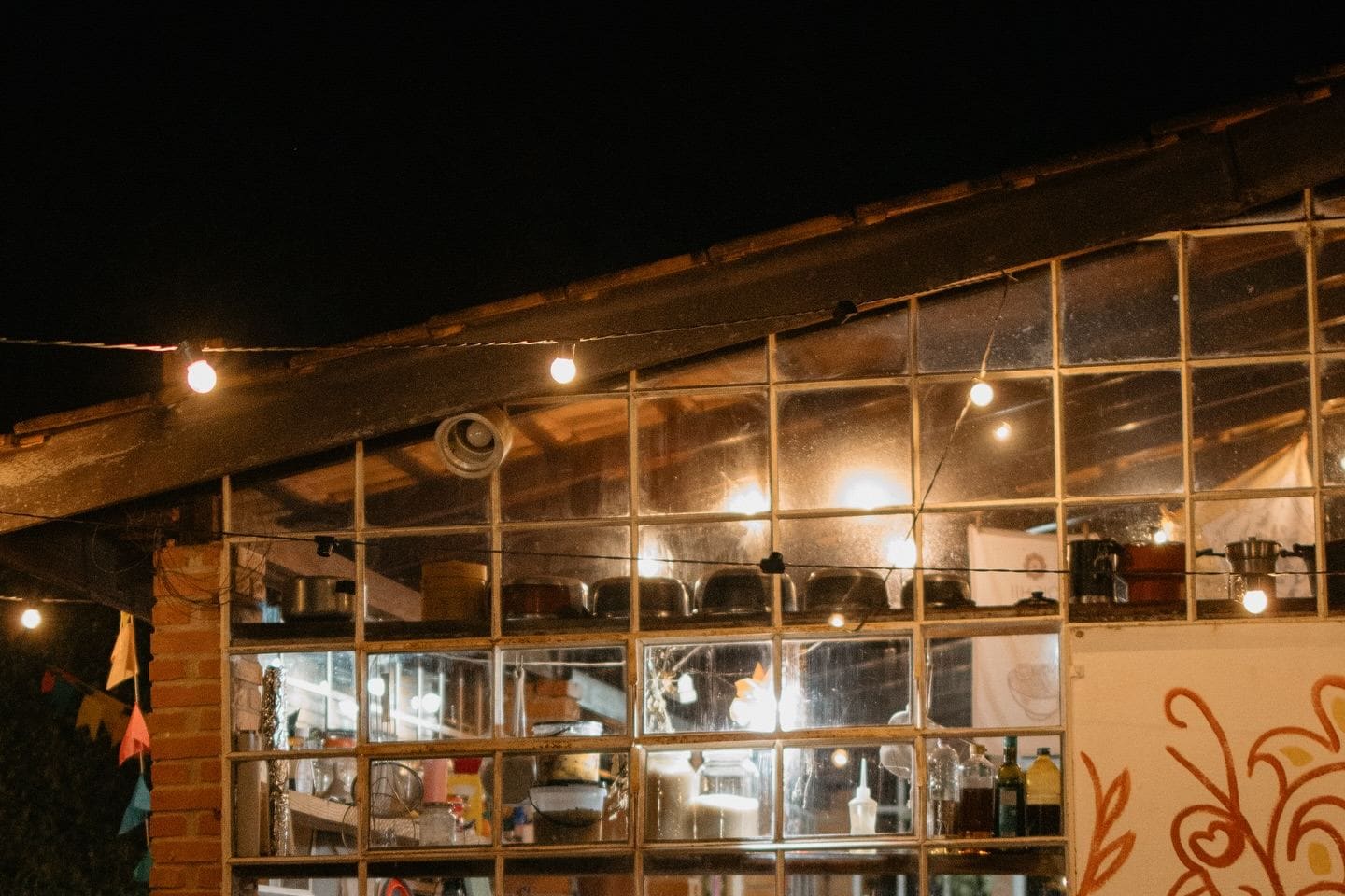 La casa del Território de noche: ladrillo, ventanas de hierro encendidas y guirnalda de luces